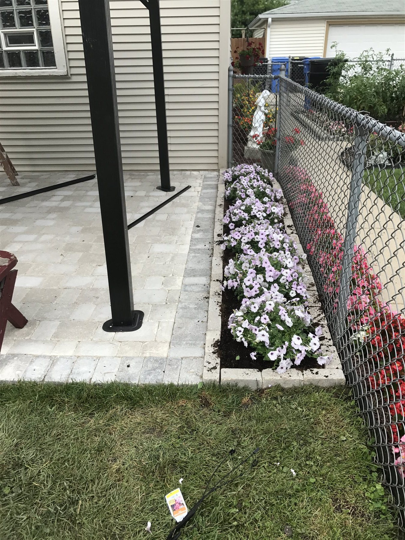 Pink and white flowers in a narrow planting bed beside a patio